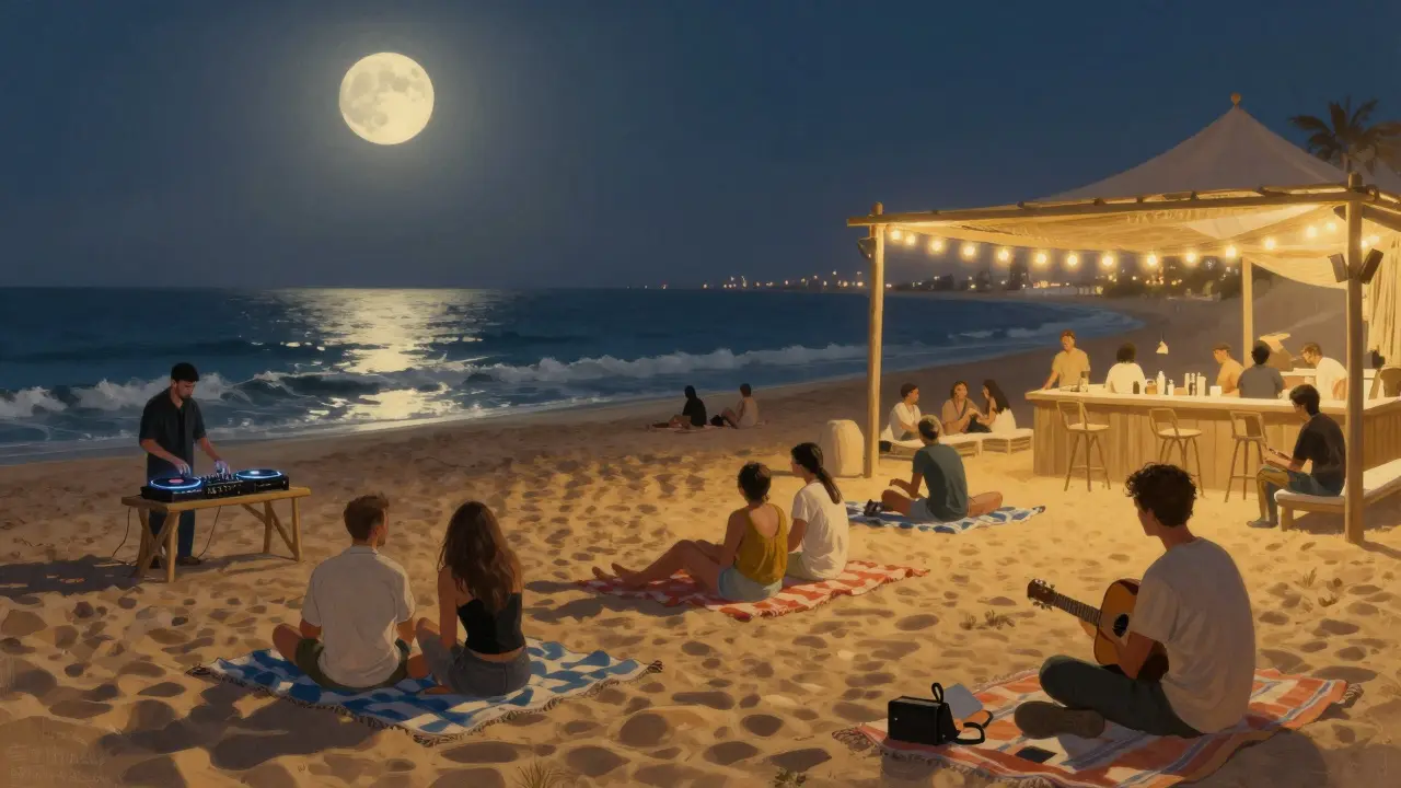 People relaxing on a beach at night with a vinyl DJ and string lights, calm waves in the background.